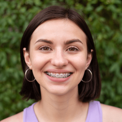 Orthodontics and your health 9 Young girl smiling and wearing braces with foliage in the background, representing orthodontics