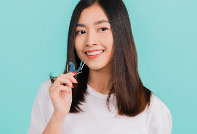 Why retainers are essential 3 Smiling woman holding dental retainer, representing how retainers keep teeth straight