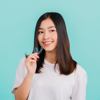 Why retainers are essential 3 Smiling woman holding dental retainer, representing how retainers keep teeth straight